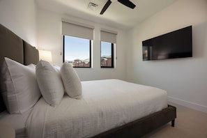 A bedroom with a bed, two windows, a ceiling fan, and a TV mounted on the wall. - AMB409 | Steamboat's Newest Luxury Complex | Pool | Hot Tub | Game Room (Steamboat Springs)