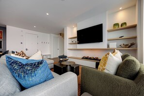 Ein modernes Wohnzimmer mit einem Flachbildfernseher, Einbauschränken und einer Sitzecke mit gemusterten Kissen.