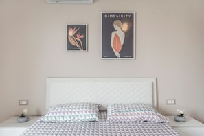Un dormitorio con una cama blanca, almohadas estampadas y dos obras de arte colgadas en la pared.
