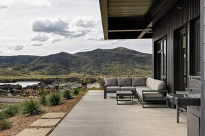 Een modern terras buiten met een bank en tafel, een barbecue, en uitzicht op een bergachtig landschap.