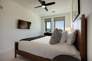 Ein Schlafzimmer mit einem Bett, einem Deckenventilator, einem an der Wand montierten Fernseher und einem Fenster mit Blick.