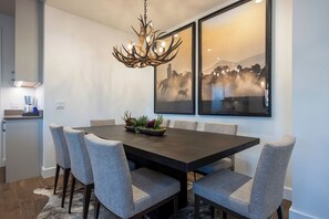 Ein Essbereich mit einem dunklen Holztisch, sechs gepolsterten Stühlen, einer Kristallleuchtre und zwei gerahmten Kunstwerken an der Wand.