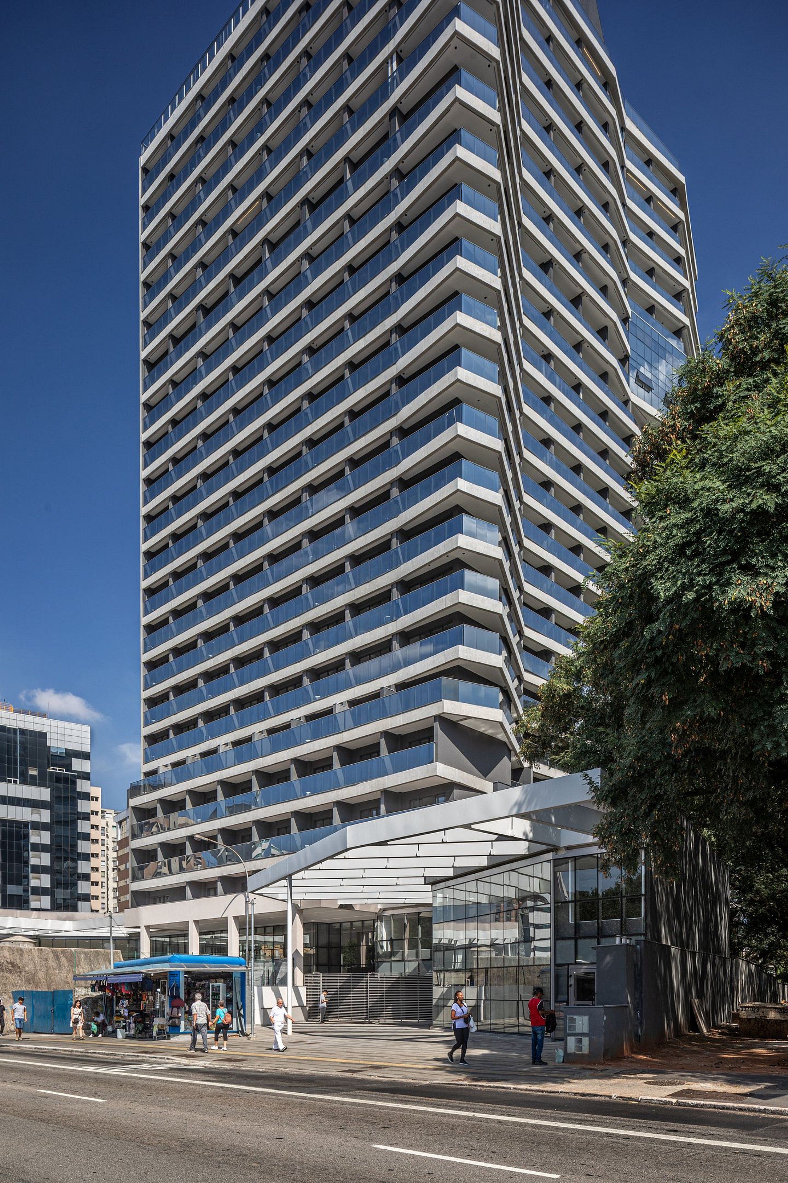 Un moderno edificio de gran altura con una fachada en zigzag distintiva y un área de acceso cubierta.