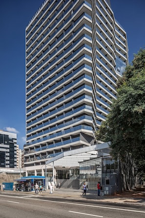 Un moderno edificio de gran altura con una fachada en zigzag distintiva y un área de acceso cubierta.