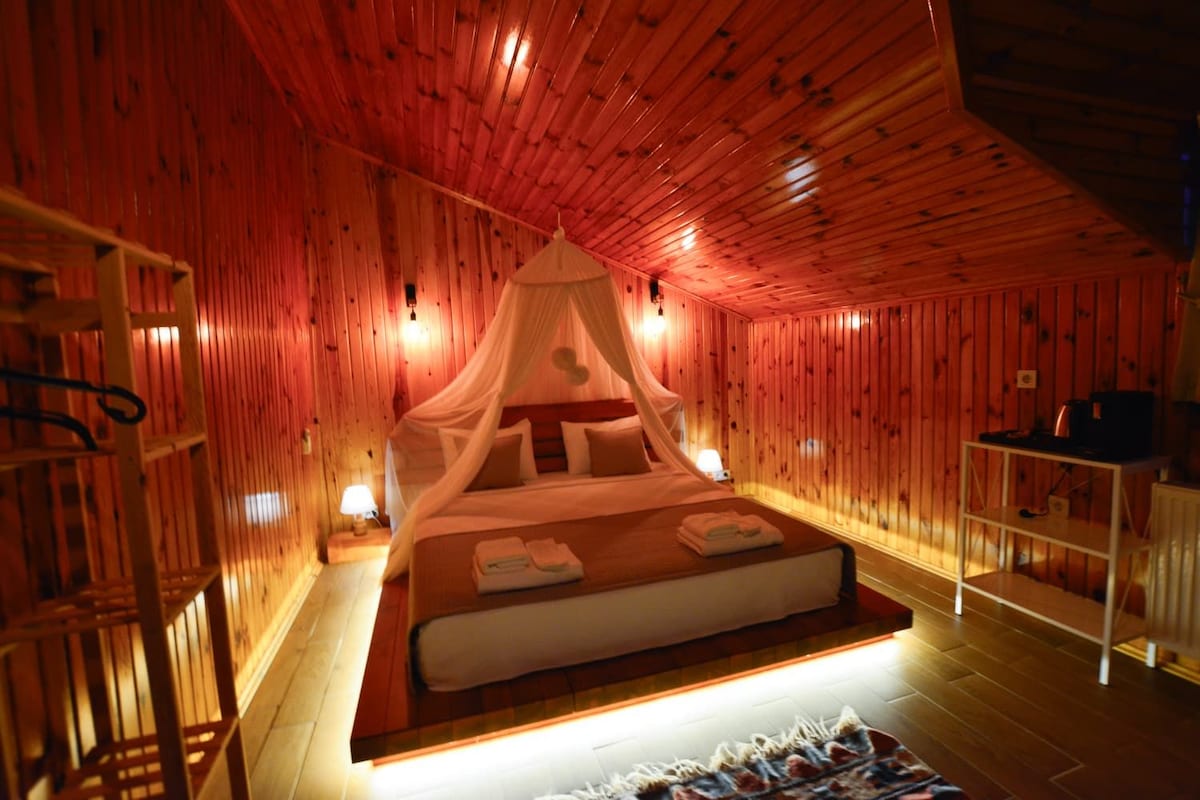 A room with a bed, a bedside table, a lamp, and a shelf with items.