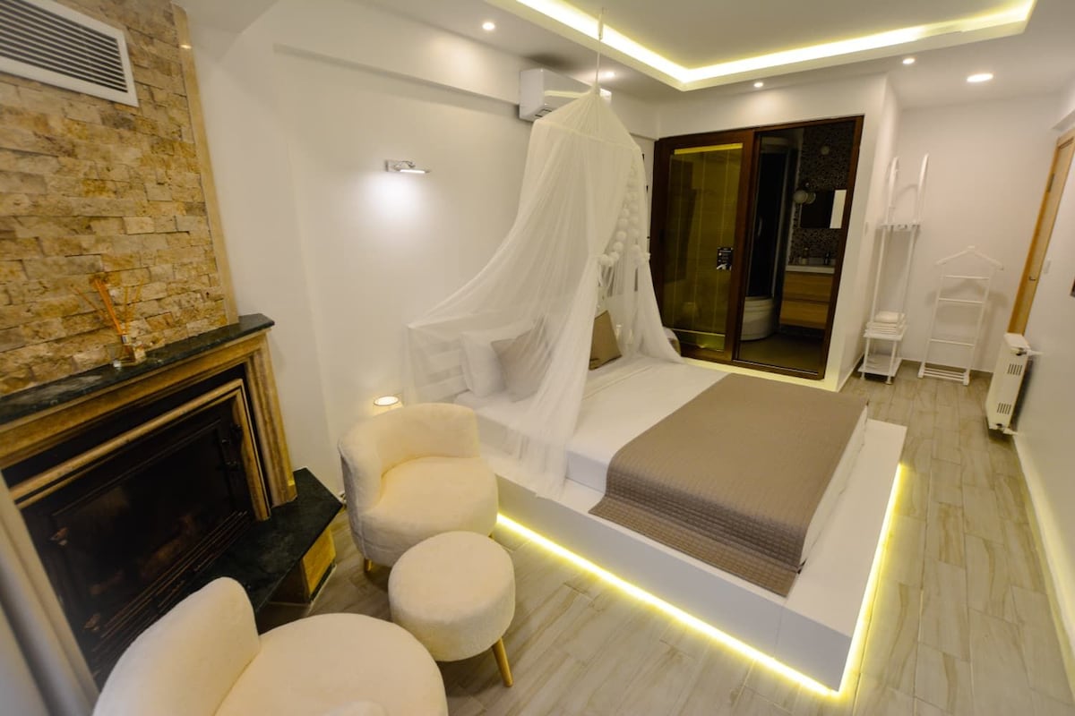 A modern bedroom with a bed, a fireplace, and a seating area.