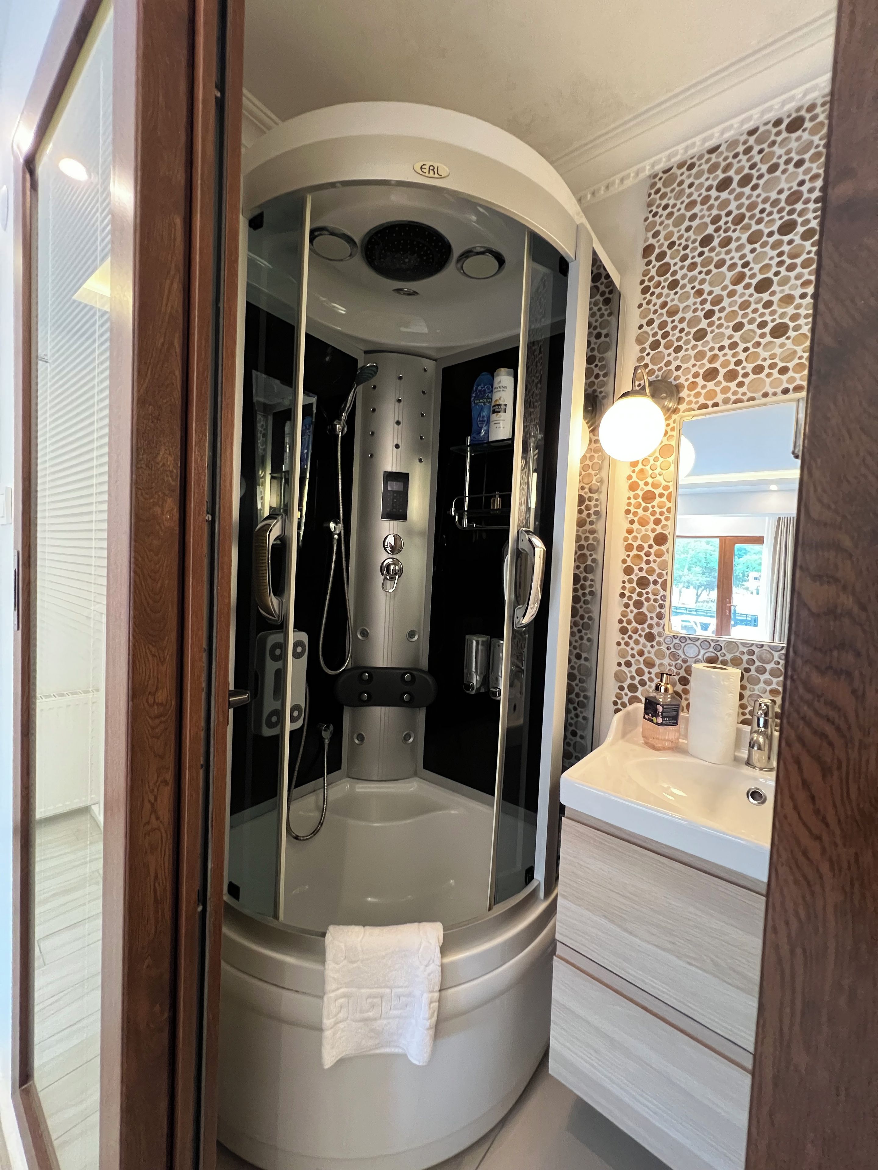 A modern bathroom with a glass-enclosed shower, a white sink, and a mirror with a decorative wall.