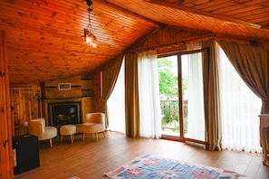 A wooden interior with a fireplace, two armchairs, a rug, and a large window with curtains. - My Dream Otel Ağva (Sile)