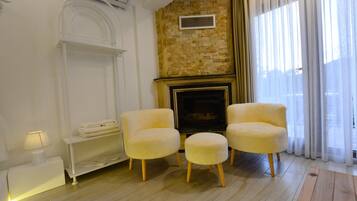 Una sala de estar acogedora con chimenea, dos sillones, una mesita auxiliar y una lámpara.