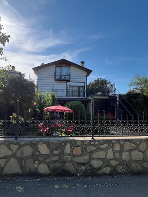 A two-story building with a stone wall in front, a red umbrella, and a staircase leading to a covered area. - My Dream Otel Ağva (Sile)