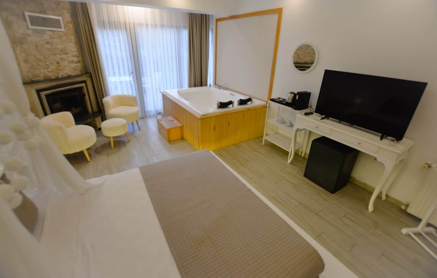 Una habitación de hotel con cama, escritorio con televisor, un pequeño rincón de descanso con sillas y chimenea.