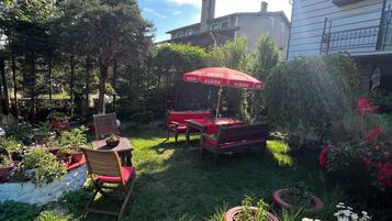 Un jardín con mobiliario exterior, un paraguas rojo y plantas en macetas.