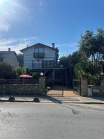 Un edificio de dos pisos con entrada protegida por un portón, un muro de piedra y un paraguas rojo.