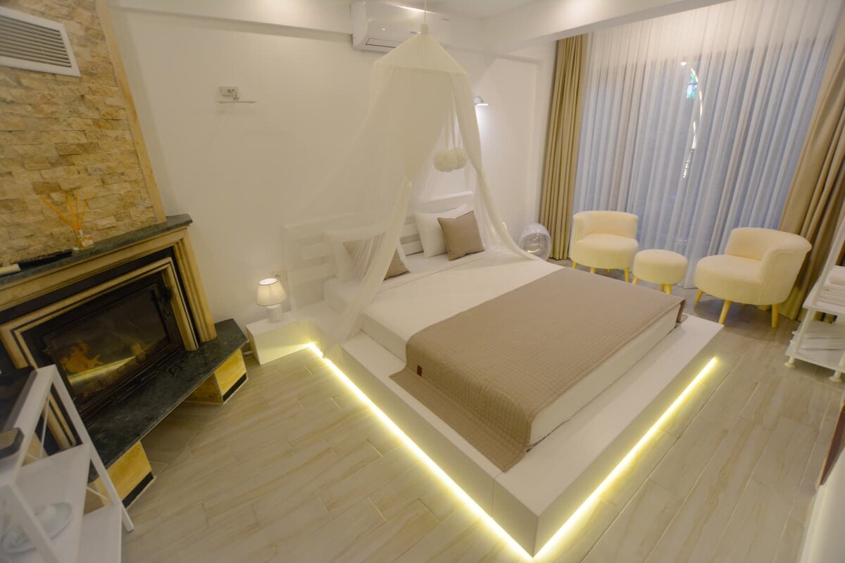 A modern bedroom with a bed, bedside tables, a fireplace, and a seating area with chairs.