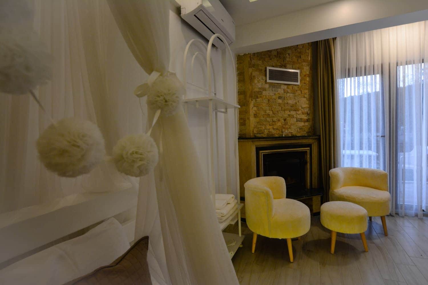Una sala de estar con chimenea, dos sillones amarillos y una cortina blanca.
