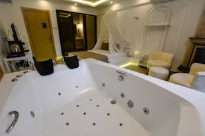 A modern bathroom with a large bathtub, a vanity with a mirror, and a seating area with a chair and a small table. - My Dream Otel Ağva (şile)