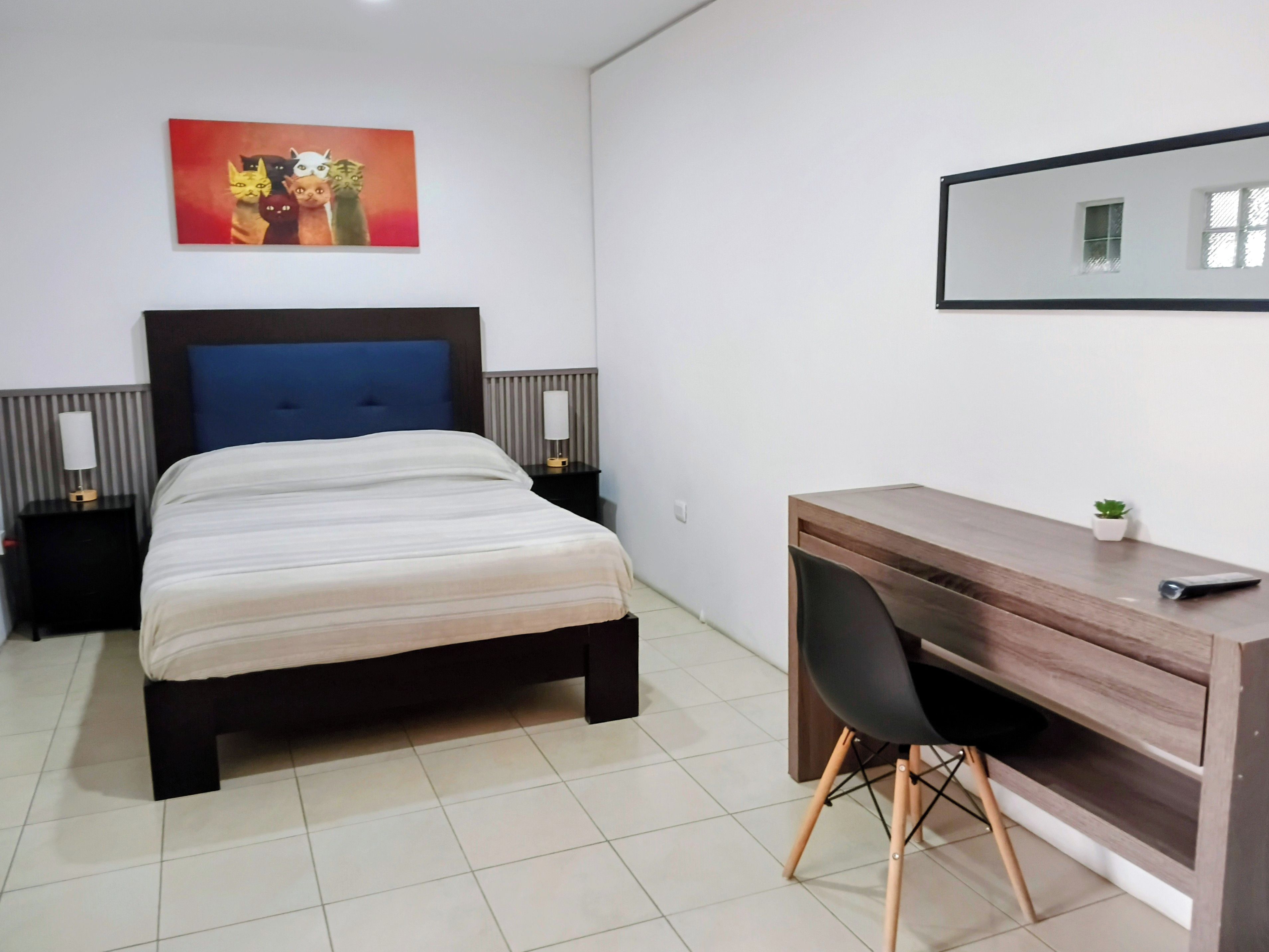 Quarto com cama, mesas de cabeceira, escrivaninha e uma cadeira.