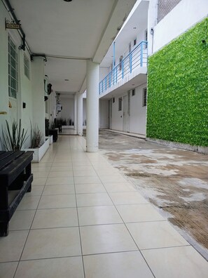 A clean, tiled corridor with a bench, potted plants, and a green wall.