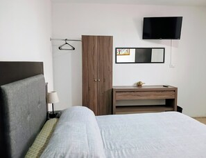 Una habitación de hotel con cama, un armario de madera, un escritorio con una pequeña figurita de tortuga, un televisor montado en la pared y un cuadro enmarcado.