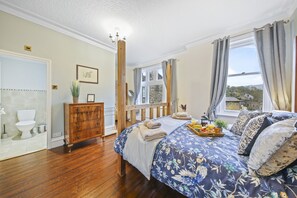 Un dormitorio con una cama de madera, un aparador, una ventana con cortinas y vistas a casas.