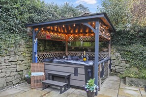 Un jacuzzi con una pérgola de madera encima, una pared de piedra y un banco.