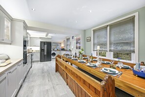 Una cocina moderna con una larga mesa de madera para seis personas, equipada con horno empotrado y refrigerador.