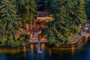 A lakeside property with a dock, a deck area with outdoor seating, and a house surrounded by dense trees.