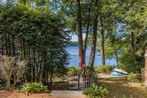 A lakeside property with a wooden deck, a red bird feeder, and a boat docked by the water. - Waterfront | Dock + Dog Friendly | Crystal Lake (Gilmanton)