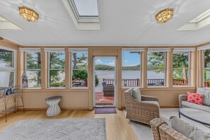 A sunroom with large windows, a fireplace, wicker furniture, and a view of a lake.