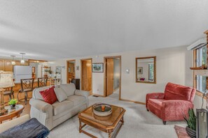 A living room with a sofa, armchair, coffee table, and a dining area with chairs and a table. - Waterfront | Dock + Dog Friendly | Crystal Lake (Gilmanton)