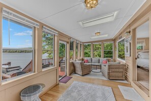 A sunroom with large windows, a wooden deck, and a seating area with wicker furniture.