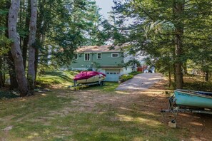 A house surrounded by trees with a boat on a trailer in the yard. - Waterfront | Dock + Dog Friendly | Crystal Lake (Gilmanton)