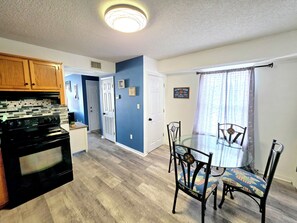 A kitchen with a black stove, wooden cabinets, and a blue wall. - Pirate’s Hideaway  3B/2.5B  Sleeps 8 Beach 1 Block (Gulf Shores)