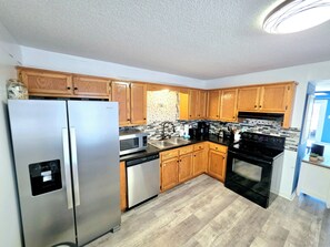 A kitchen with wooden cabinets, a stainless steel refrigerator, a microwave, a dishwasher, a sink, and a stove. - Pirate’s Hideaway  3B/2.5B  Sleeps 8 Beach 1 Block (Gulf Shores)