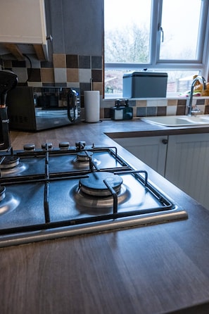 A kitchen with a gas stove, a microwave, and a coffee maker. - Modern home, ideal for long stays Free Parking (West Sussex)