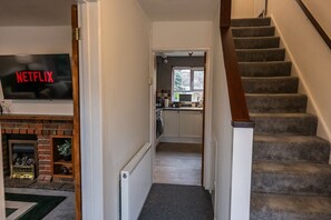 A hallway leading to a kitchen with a fireplace, a staircase, and a TV displaying the Netflix logo. - Modern home, ideal for long stays Free Parking (West Sussex)