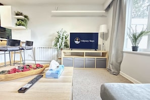 A living room with a flat-screen TV, a wooden coffee table with a remote control, a sofa, and a potted plant. - Cosy Horsham 1-Bed · Free Parking · Walk to Town (Horsham)