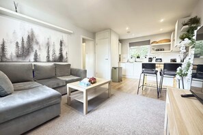 A modern living room with a grey sofa, a coffee table, and a kitchen area with a dining table and chairs. - Cosy Horsham 1-Bed · Free Parking · Walk to Town (Horsham)