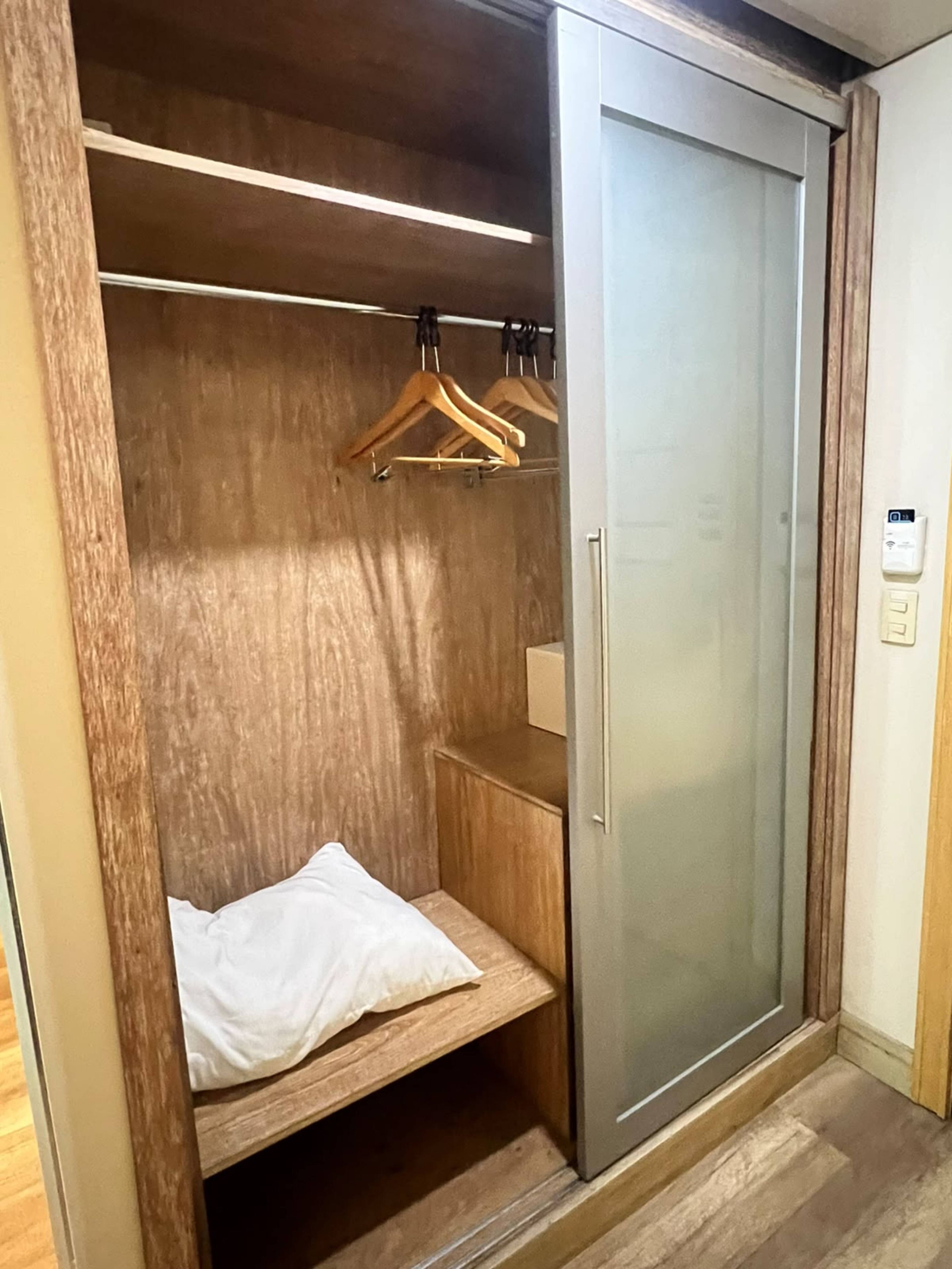 Een inloopkast met houten planken, een kledingrek en een bed met een wit kussen.