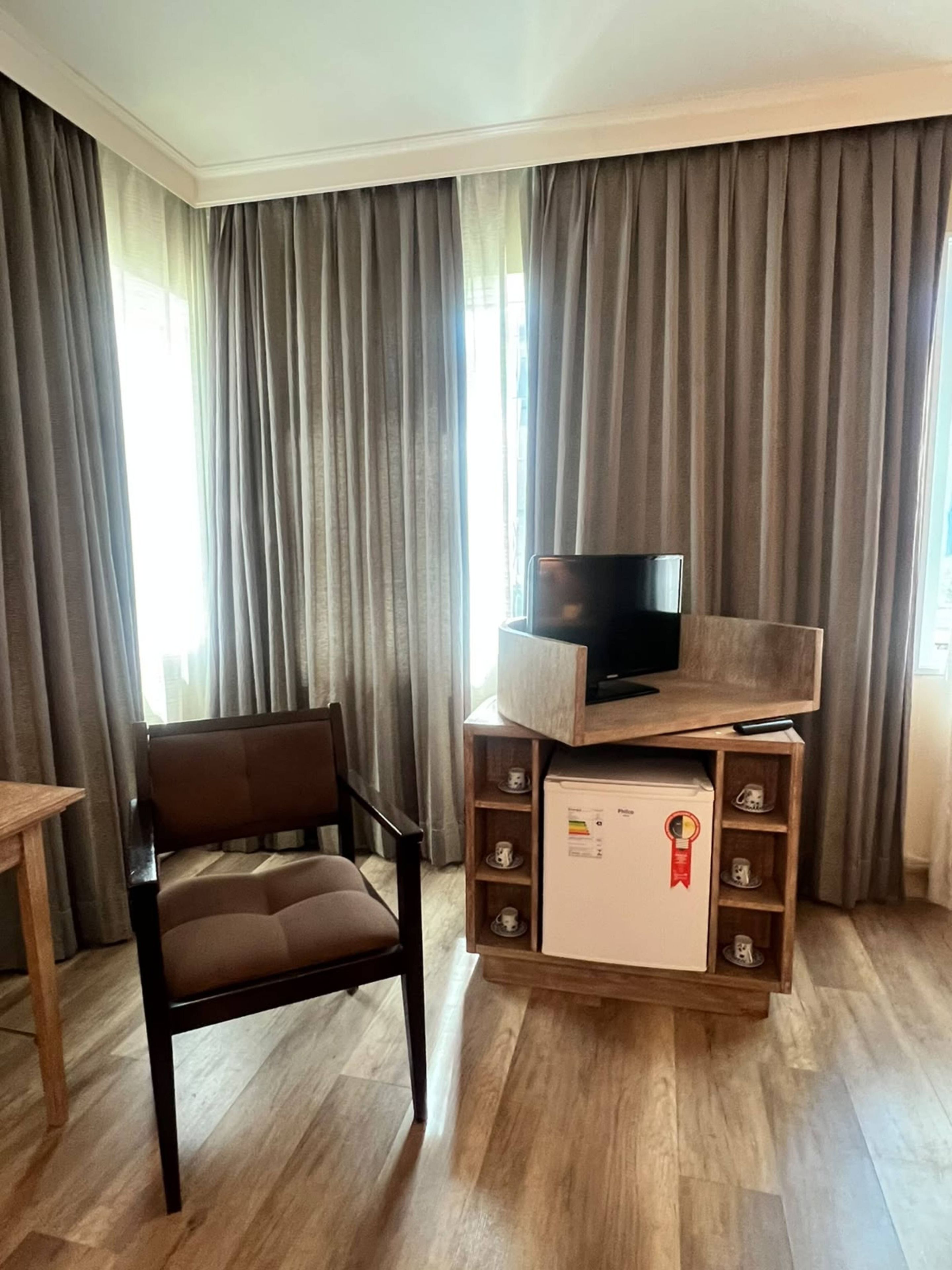 Une pièce avec un téléviseur posé sur un meuble en bois, une chaise et un mini-réfrigérateur orné d’un autocollant rouge.