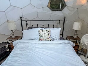 Un lit avec une literie blanche, un coussin décoratif et deux tables de chevet avec des lampes.