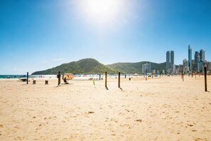 Ein Strand mit Volleyballnetzen, einem Sandufer und einer Skyline mit hohen Gebäuden im Hintergrund.