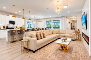 A modern living room with a large L-shaped sofa, a marble coffee table, and a fireplace. - 10BR Home with Game Room Near Disney 49LA (Davenport)