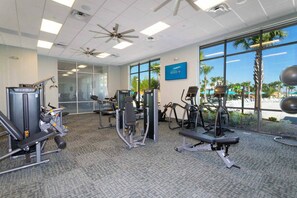 Una palestra con attrezzature per esercizi, ampie finestre e vista su palme.