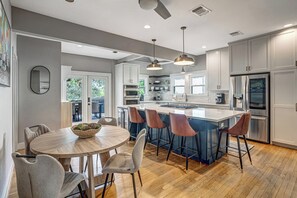 A modern kitchen with a central island, bar stools, and a dining table with chairs. - Minutes to SoCo - Sleeps 10 w Studio, Near DT (Austin)