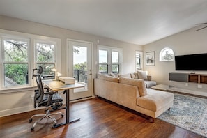 A spacious living room with a large window, a sofa, a coffee table, and a flat-screen TV. - Minutes to SoCo - Sleeps 10 w Studio, Near DT (Austin)