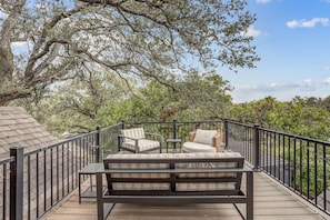 A wooden deck with a black metal railing, a cushioned bench, and two wicker chairs. - Minutes to SoCo - Sleeps 10 w Studio, Near DT (Austin)