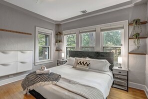 Ein Schlafzimmer mit einem großen Bett, zwei Nachttischen, einer Kopfteil und mehreren Fenstern.