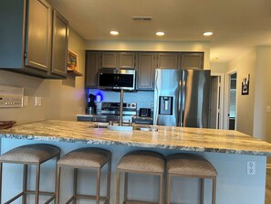A modern kitchen with stainless steel appliances, a marble countertop, and bar stools. - Monterey Bay - Three Bedroom Apartment, Sleeps 8 (Village of Four Seasons)
