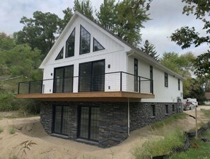 A modern two-story house with a stone foundation, large windows, and a balcony. - Lake Gogebic Chalet at Cabin Creek (MARENISCO)